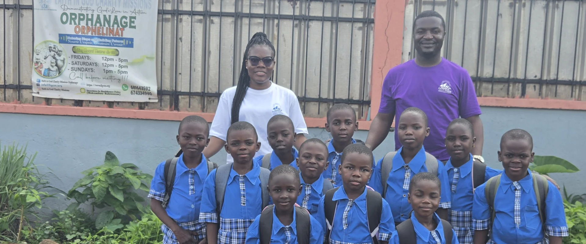 Schoolchildren in blue uniforms with backpacks, with two FIGCM staff members, outside the orphanage.