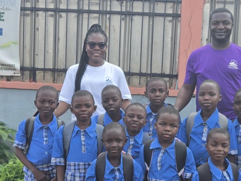 Schoolchildren in blue uniforms with backpacks, with two FIGCM staff members, outside the orphanage.